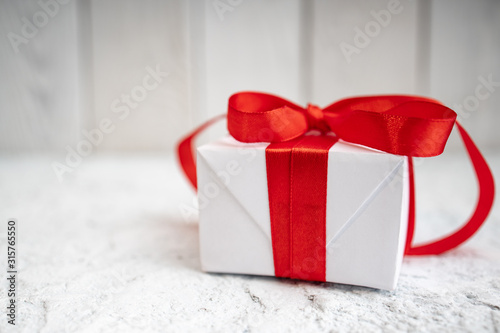 Gift box for Valentine's Day. View of present box package decorated into the white paper and red bow-knot. Flat lay on white background. ..