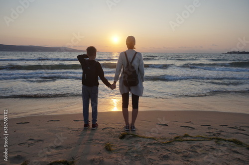 Strong for family. Mom and son meet the dawn on the sandy seashore