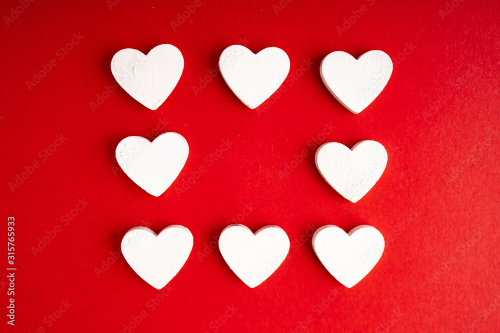 Top view of white wooden hearts on the red paper background. Flat lay for Valentine's Day. Concept of love...