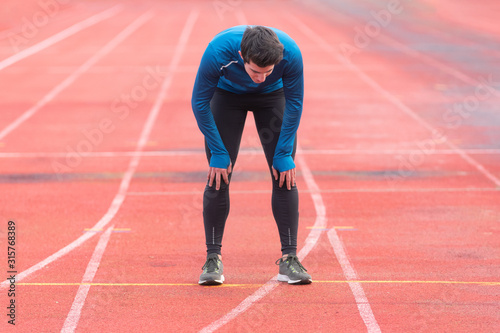 Athlete young man tired, resting on running track .
