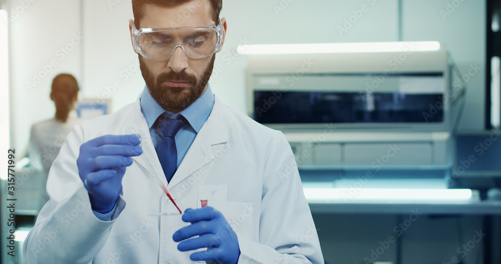 Caucasian young man laboratory scientist in glasses making a blood test with a tube in hands. Portrait. Close up - obrazy, fototapety, plakaty 