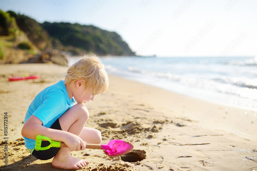Little boy playing with shovel on sand beach near seashore in Greece Little boy playing with shovel on sand beach near seashore in Greece