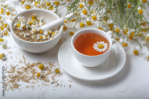 Rural still-life - cup of brewed chamomile tea on the background of a bouquet of daisies, closeup
