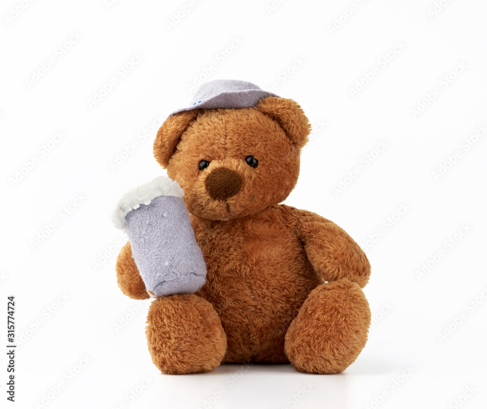 Fototapeta premium cute little brown teddy bear holds a felt mug with foam and is dressed in a gray hat