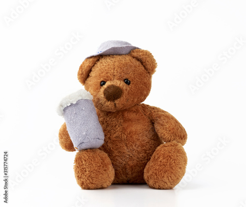 cute little brown teddy bear holds a felt mug with foam and is dressed in a gray hat