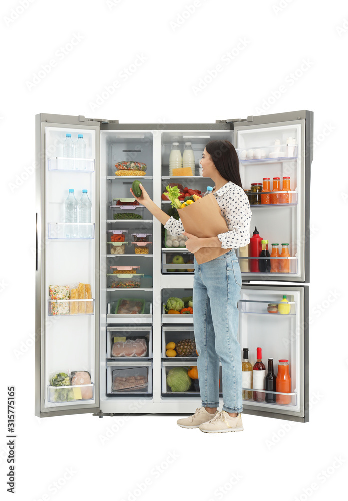Young woman with bag of groceries near open refrigerator on white background Young woman with bag of groceries near open refrigerator on white background