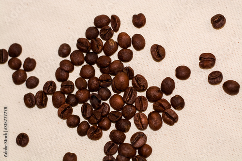One-tone light background of coarse fabric. Arabica coffee beans are scattered. Caffeine drink.