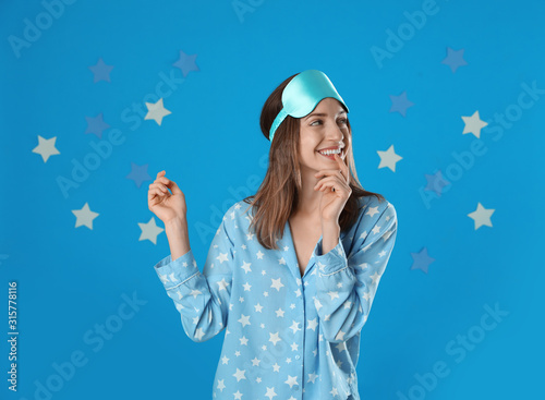 Beautiful woman wearing pajamas and sleep mask on light blue background. Bedtime photo