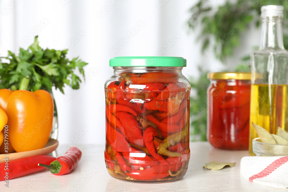 Glass jar of pickled pickled peppers on white table Glass jar of pickled pickled peppers on white table