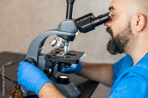 Male laboratory assistant examining biomaterial samples in a microscope.