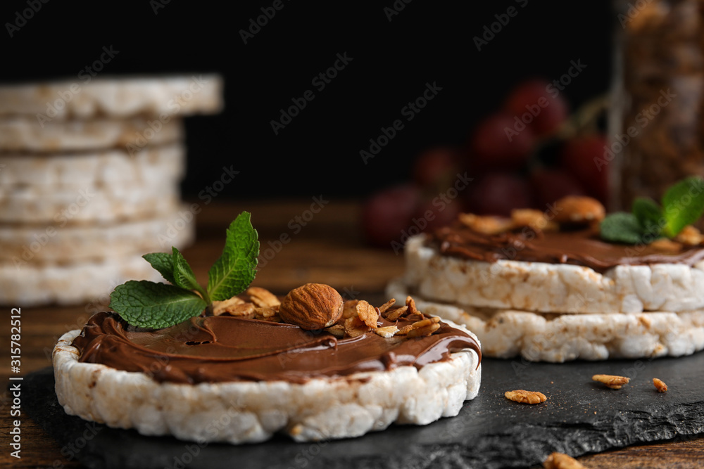 Fototapeta premium Puffed rice cakes with chocolate spread, nuts and mint on slate board, closeup