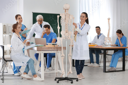 Medical students and professor studying human skeleton anatomy in classroom