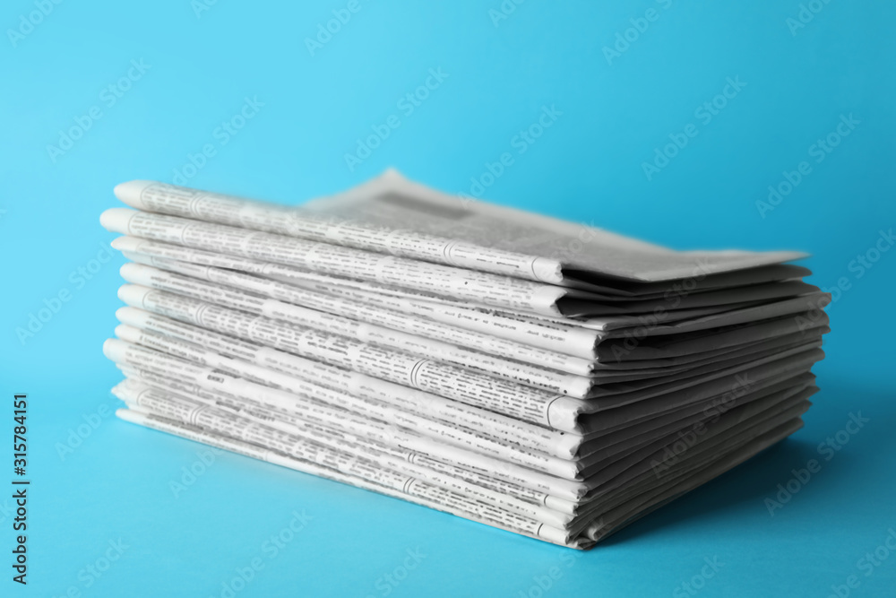 Stack of newspapers on light blue background. Journalist's work