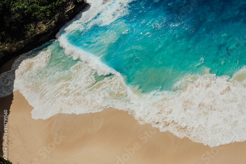 Angled shot of bright cerulean waves crashing into the shore