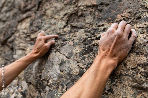 Closeup perspective on a rock climber ascending a limestone cliff in nature. White chalk covering hands and fingers to dry sweat and increase friction