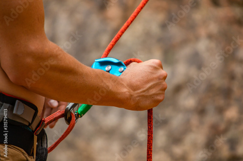 A close up view on the muscular arms of a rock climber, using hands to fix climbing rope to a safety harness. Professional sports gear with copy space