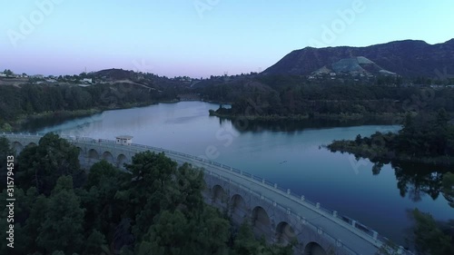 Aerial over trees and water of Hollywood reservoir lake, in soft blue and pink morning light, Los Angeles