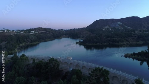 Aerial descent over the Hollywood Reservoir dam in soft blue and pink morning light, Los Angeles
