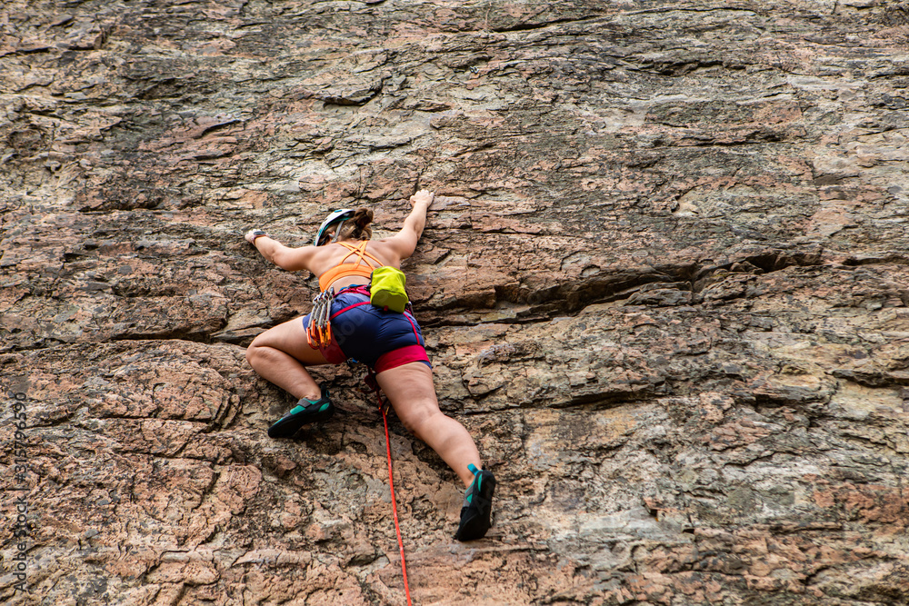 A low angle view of a healthy caucasian woman wearing specialized sportswear with helmet and gear belt. during a rock climbing activity outdoors