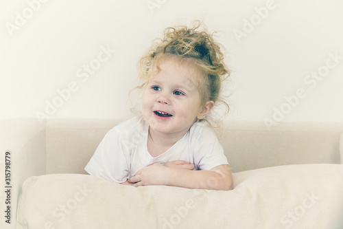 The little girl laughs sitting on the couch.