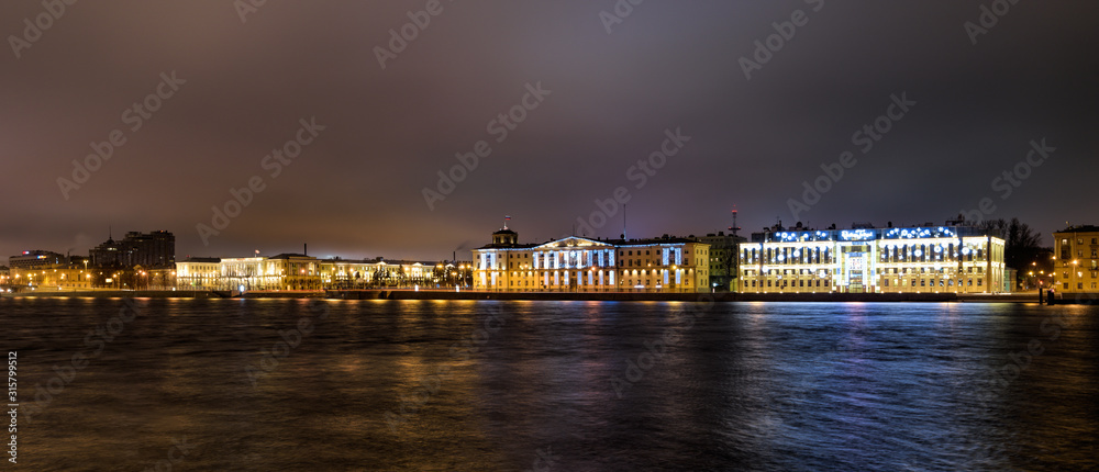 Night panorama of bright colorful Neva river embankment at snowless winter. Saint-Petersburg, Russia.