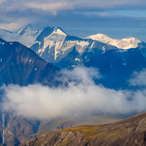 Mountain landscape, morning light. Snow-capped peaks rise above the clouds. © Valerii