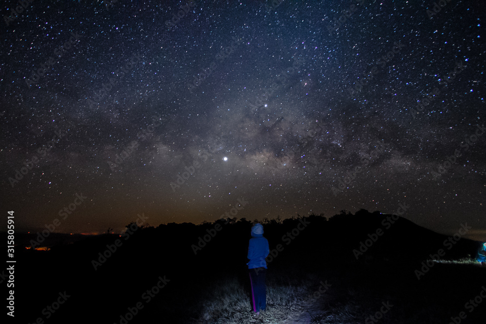 milky way in night sky with woman standing in background