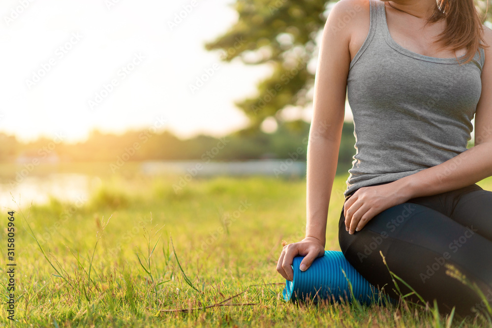 Young asian woman wearing exercise suit and sit on blue yoga mat or fitness mat after practicing yoga in park, Healthy concept, Mind-body improvements concept.