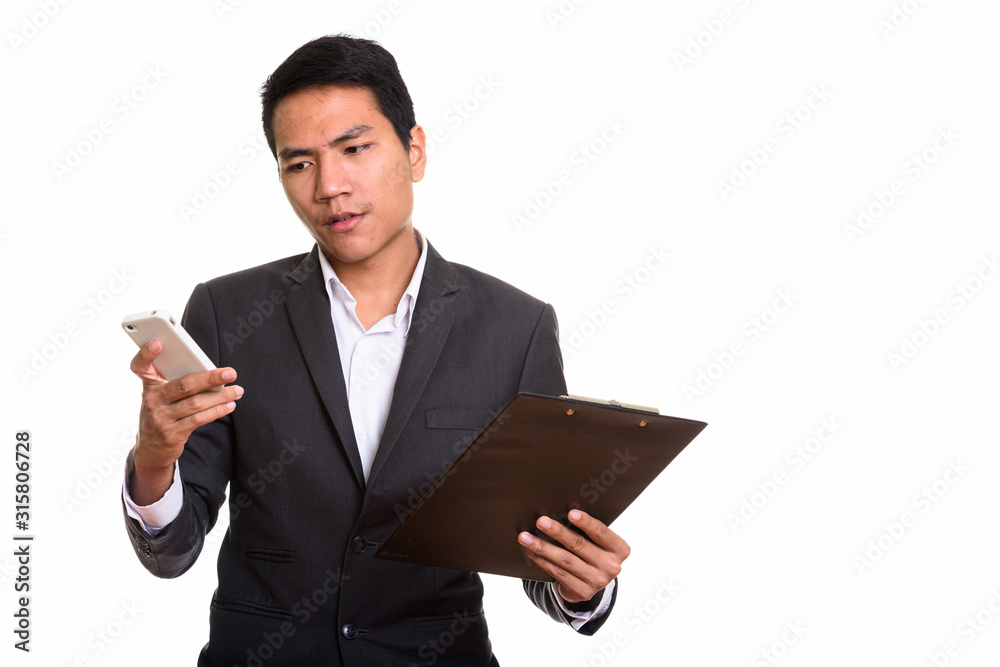 Studio shot of young Asian businessman using mobile phone while Studio shot of young Asian businessman using mobile phone while