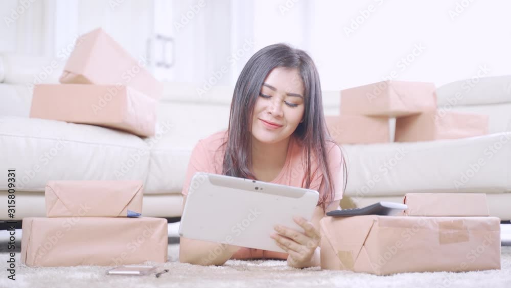 Pretty online shop owner working with tablet and talking on the mobile phone while lying on the carpet in the living room at home. Small Medium Enterprise or Start up concept. Shot in 4k resolution Pretty online shop owner working with tablet and talking on the mobile phone while lying on the carpet in the living room at home. Small Medium Enterprise or Start up concept. Shot in 4k resolution