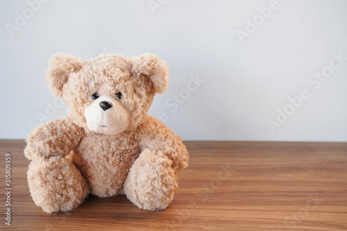 Cute Teddy Bear sitting alone with white cement wall on wooden table