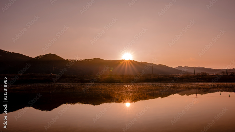 The sun rising over the mountains and the sun reflected in the river.