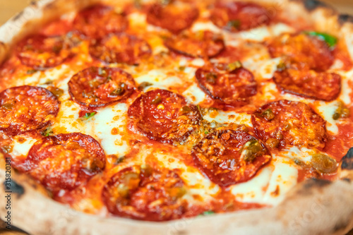 Freshly baked pizza with salami, cheese, sauce, vegetables and meat on a wooden table