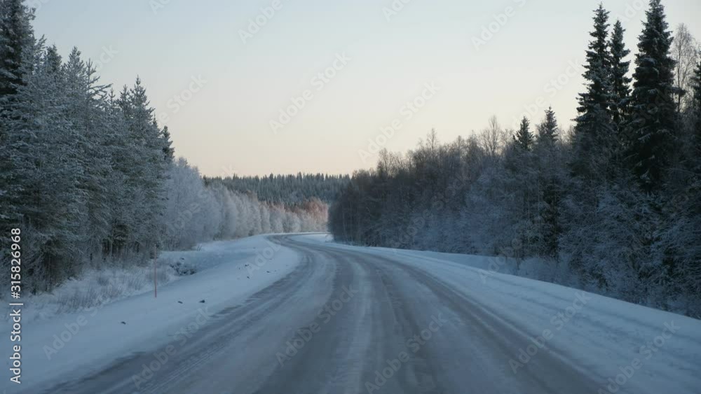 Frosty and snaky highway wriggling gradually in a dense pine forest in Finland Frosty and snaky highway wriggling gradually in a dense pine forest in Finland