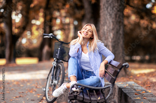 Girl sitting on bench in park with bicycle on background