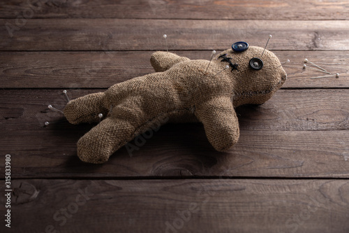 Voodoo doll on a wooden background with dramatic lighting. The concept of witchcraft and black art. Burlap doll on a wooden background. Pierce with maces. Copy space.