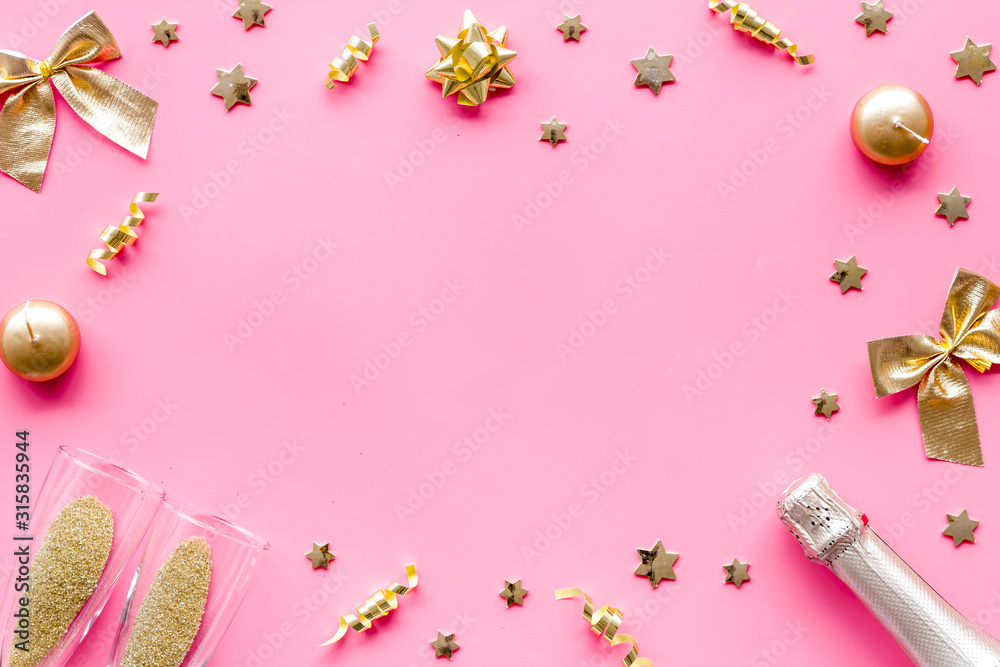 New Year mockup in gold color. Champagne bottle, present box, decoration, balls on pink background top-down frame copy space