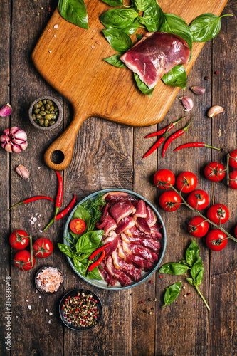 Smoked roasted goose carpaccio on wooden table with garnish green salad
