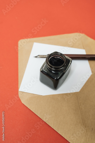 Set of vintage dip pen, inkpot and blank paper sheet on red background