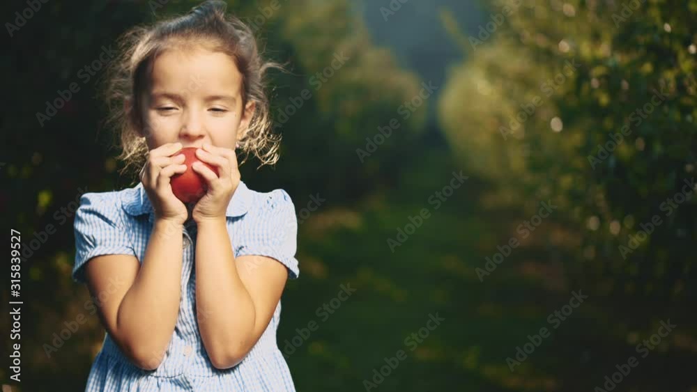 Hungry girl is biting a red apple outdoors. Girl is smiling widely. Close up. Copy space. 4K. Hungry girl is biting a red apple outdoors. Girl is smiling widely. Close up. Copy space. 4K.