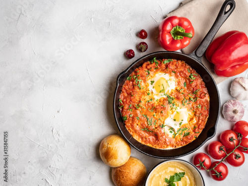 Shakshuka with bell pepper, tomatoes, hummus and rolls. Top view, place for text.