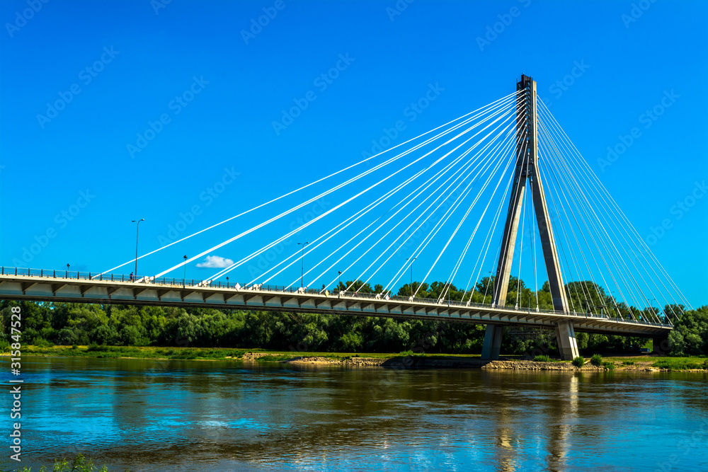 Fototapeta premium Modern bridge in Warsaw. Sunny summer day with a blue sky and green trees. Horizontal photo.