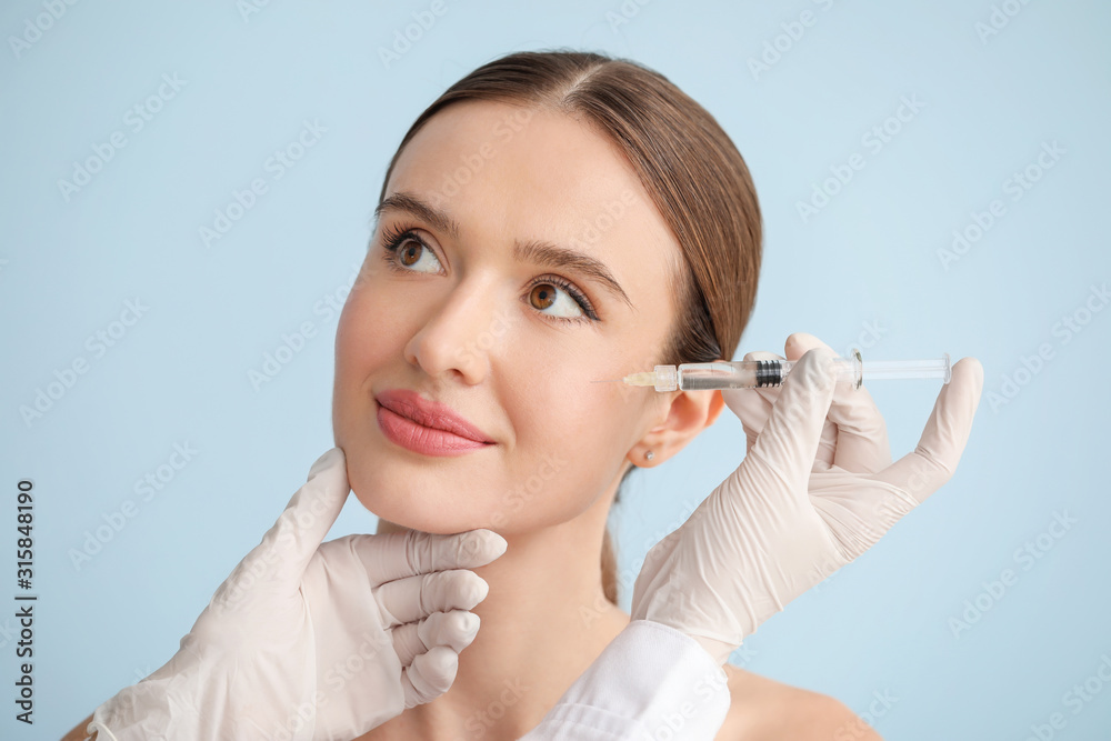 Young woman receiving filler injection against color background Young woman receiving filler injection against color background
