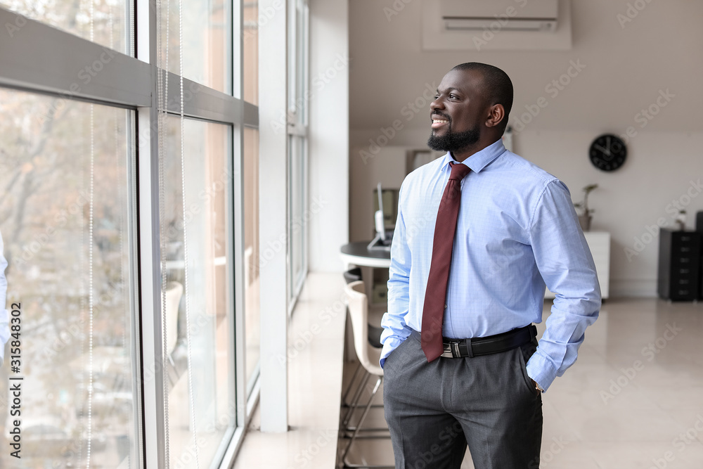 Portrait of handsome African-American businessman near window in office