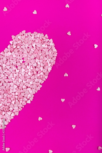 Bright pink background. Pink half a heart on a pink background. Hearts sprinkles. Valentine day. Flat lay style. Top view. Sweet background. Confetti.