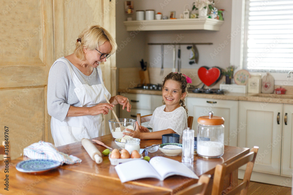 Horizontal view. Grandmother and nephew have fun in the kitchen making together, kneading dough. Horizontal view. Grandmother and nephew have fun in the kitchen making together, kneading dough.