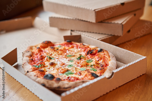 Pizza delivery concept. Baked products in a cardboard box against a wooden background. Baked tasty margherita pizza in Traditional wood oven in Neapolitan restaurant, Italy.