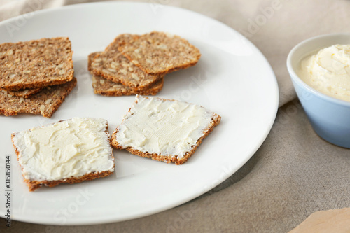 Plate with fresh bread and tasty cream cheese on table
