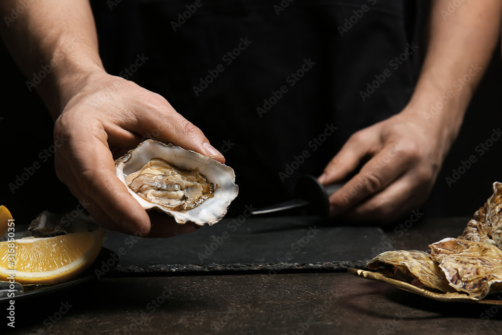 Man opening shell of fresh oyster on dark background