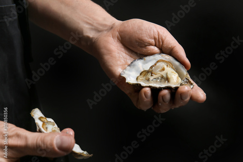 Man opening shell of fresh oyster on dark background